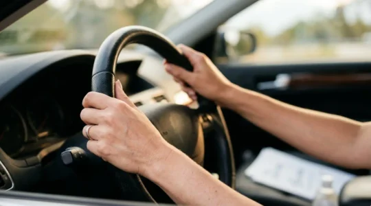 Main tenant un volant de voiture avec document d'assurance automobile, symbolisant la recherche d'une nouvelle assurance après résiliation