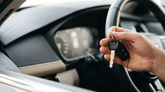 Vue rapprochée d'une main tenant des clés de voiture devant un tableau de bord moderne, symbolisant le choix d'assurance pour un véhicule