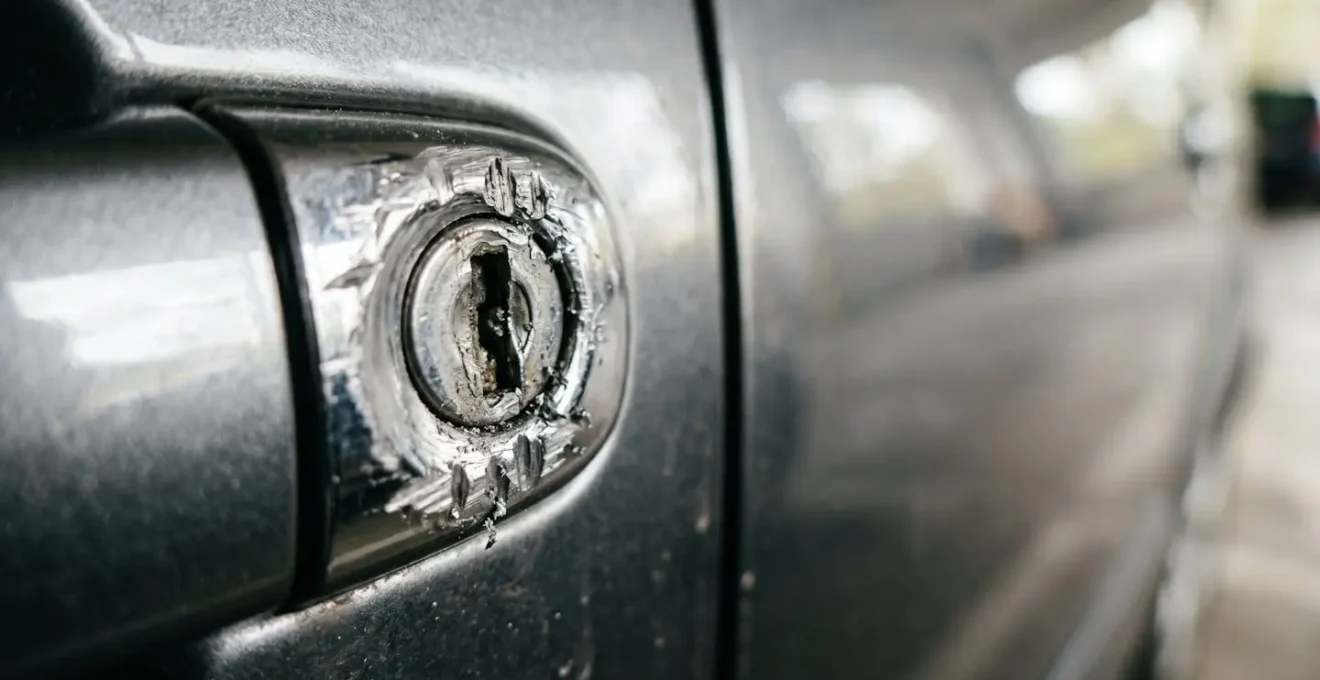 Gros plan sur une serrure de portière de voiture endommagée révélant des traces d'effraction avec des marques d'outils métalliques, illustrant une tentative de vol automobile