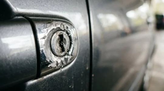 Gros plan sur une serrure de portière de voiture endommagée révélant des traces d'effraction avec des marques d'outils métalliques, illustrant une tentative de vol automobile